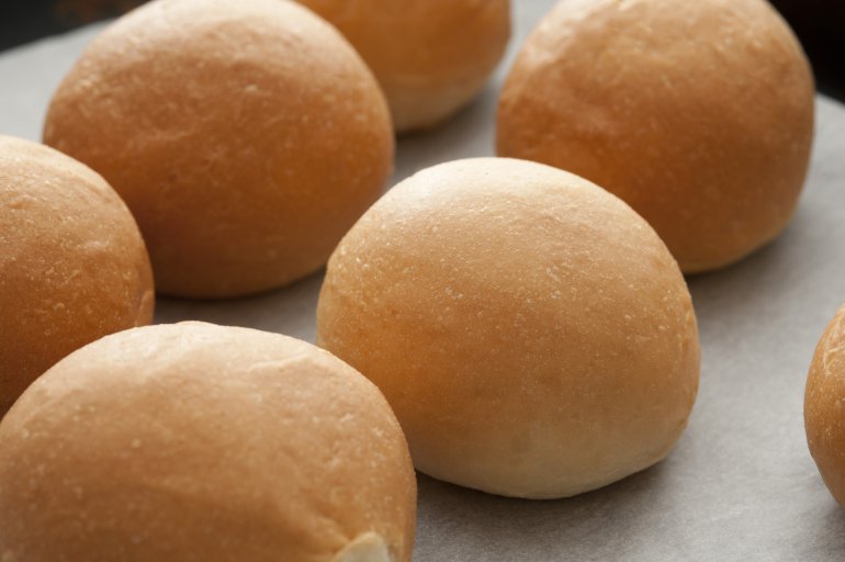Close up view of a batch of fresh crusty round white brioche rolls laid out in rows