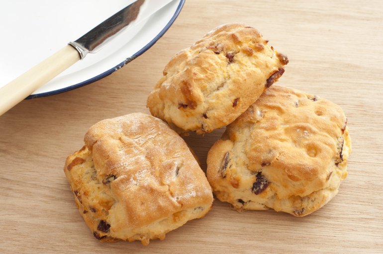 Three freshly baked delicious homemade scones with raisins on a wooden kitchen counter alongside a plate and knife