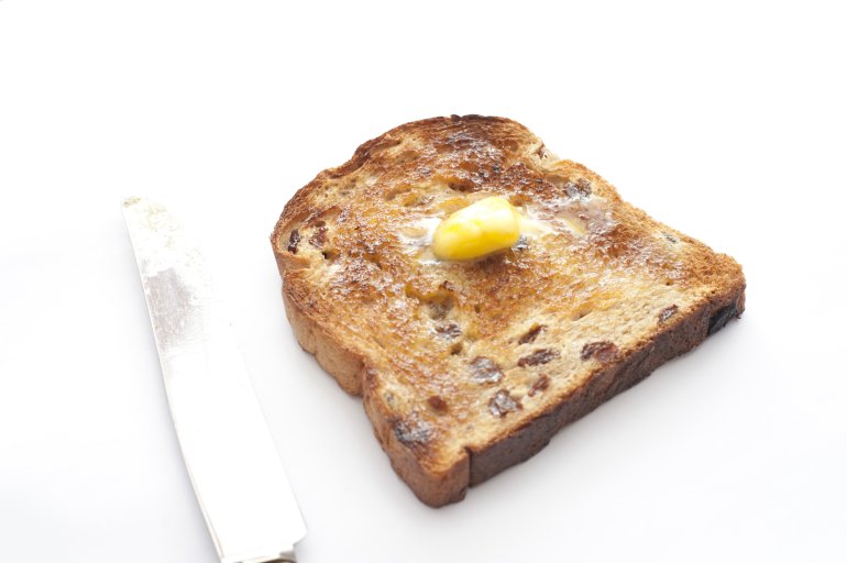 Slice of hot fruity toast with raisins and a dollop of melting butter on top on a white background, high angle view