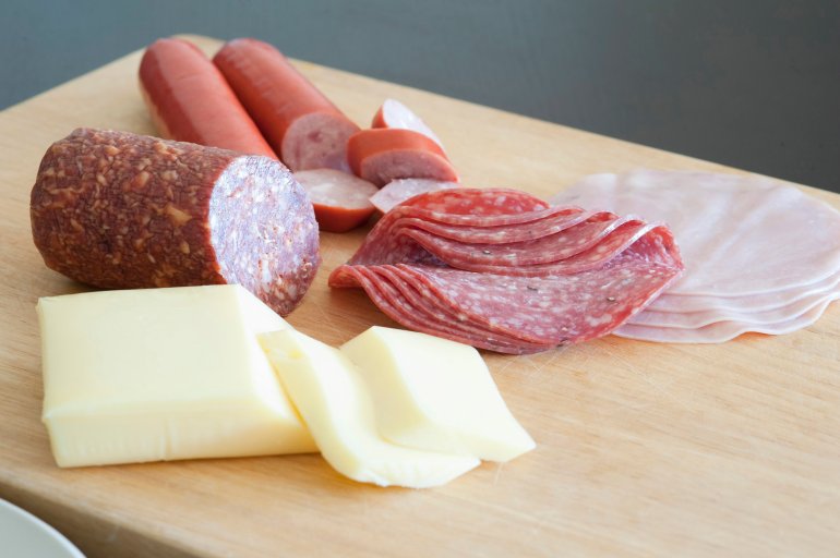 German breakfast laid out on a wooden chopping board with thinly sliced salami and cold meats and portions of fresh cheese