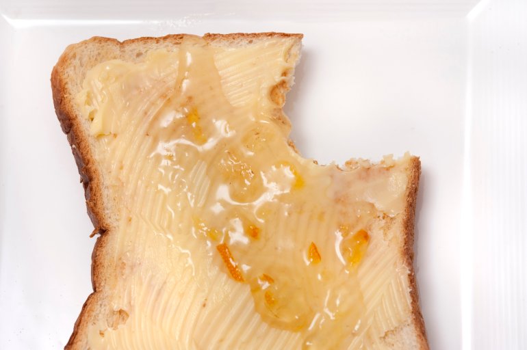 Single slice of white breakfast toast topped with butter and marmalade with a bite taken out of one corner, overhead view