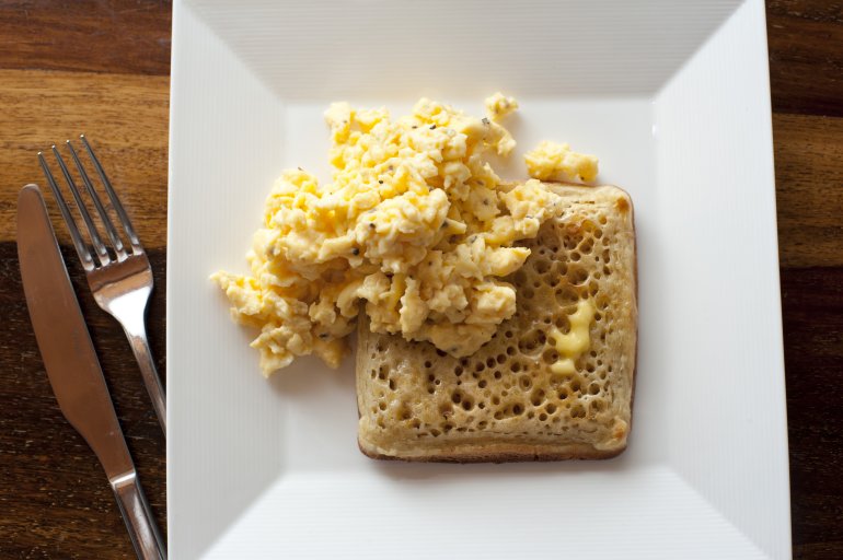 Top down view on light scrambled eggs and crumpet bread breakfast in square plate beside knife and fork
