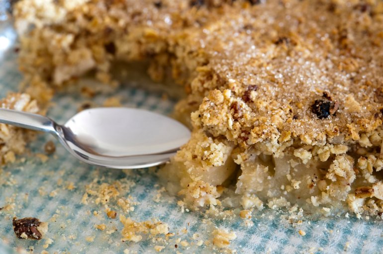Freshly baked delicious fruity apple crumble with cinnamon and raisins in a serving dish with a spoon