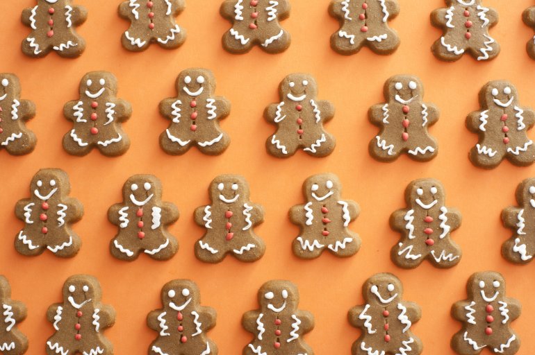 Full frame of gingerbread men cookies with white and red icing details lined up and spaced evenly over orange background