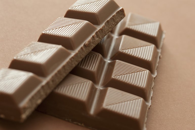 Broken bar of milk chocolate candy with a textured lined pattern on the individual square on a brown background, low angle view