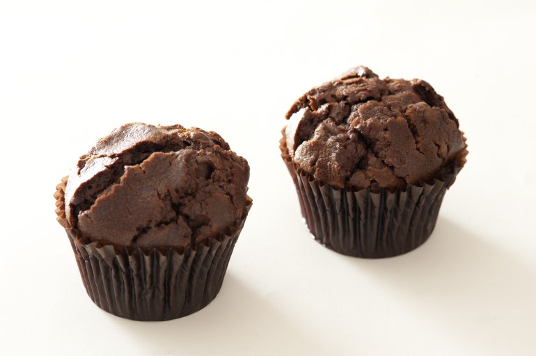 Pair of yummy baked chocolate muffins with cracked tops and subtle shadows over white background