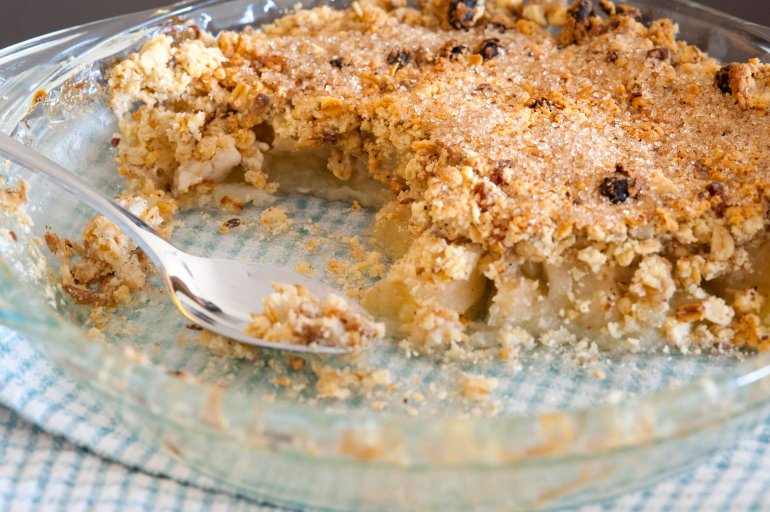 Freshly baked apple crumble dessert topped with spicy crumble with raisins in a glass pie plate