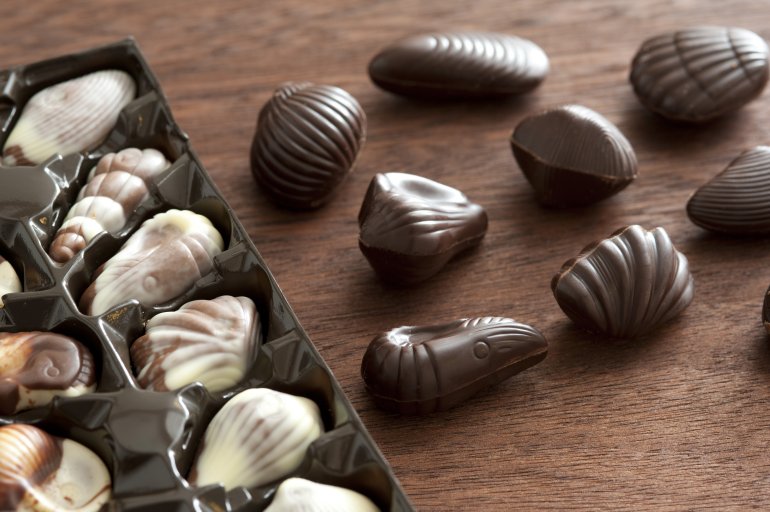 Assorted speciality shell shaped chocolates in dark chocolate, milk chocolate and white chocolate, some in the original packaging and others alongside on a wooden table