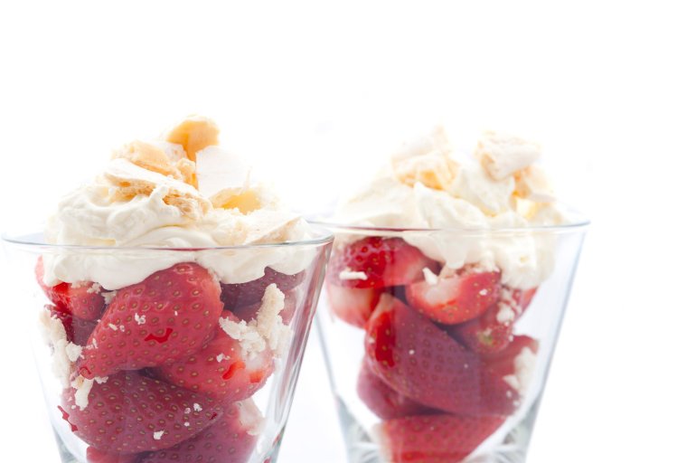 Close up view of ripe red luscious strawberries served with whipped cream in tall glasses isolated on white