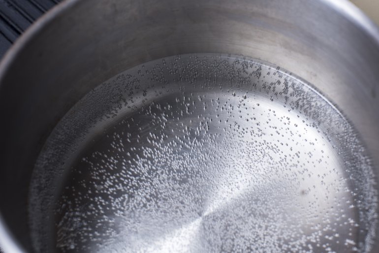 Overhead view of water beginning to boil in a stainless steel quart sized pot