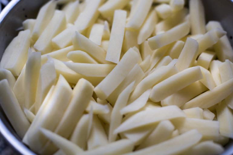 Close up overhead view of cut white potatoes shaped as sticks piled in mixing bowl
