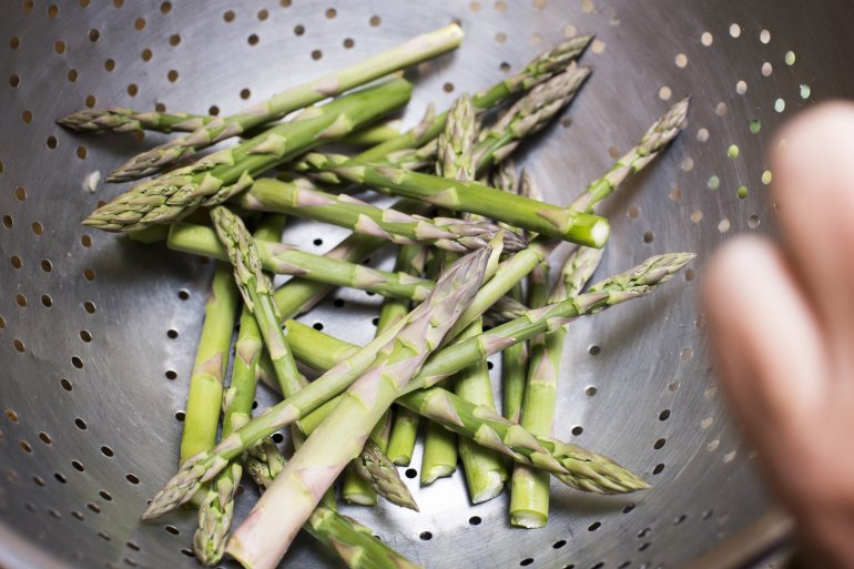 Man washing fresh green asparagus tips in a stainless steel colander before cooking them for dinner