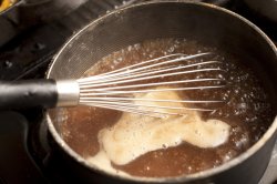 Metal whisk resting over a pot of boiling gravy