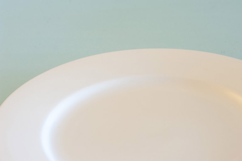 Partial view of an empty clean white dinner plate over a blue background for food placement
