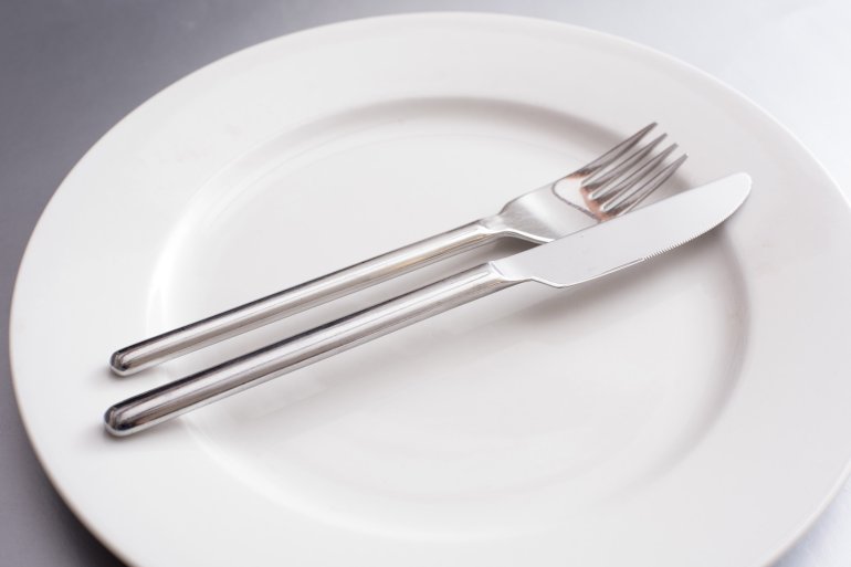 Plain generic silver metal knife and fork on a clean empty white dinner plate in a close up view