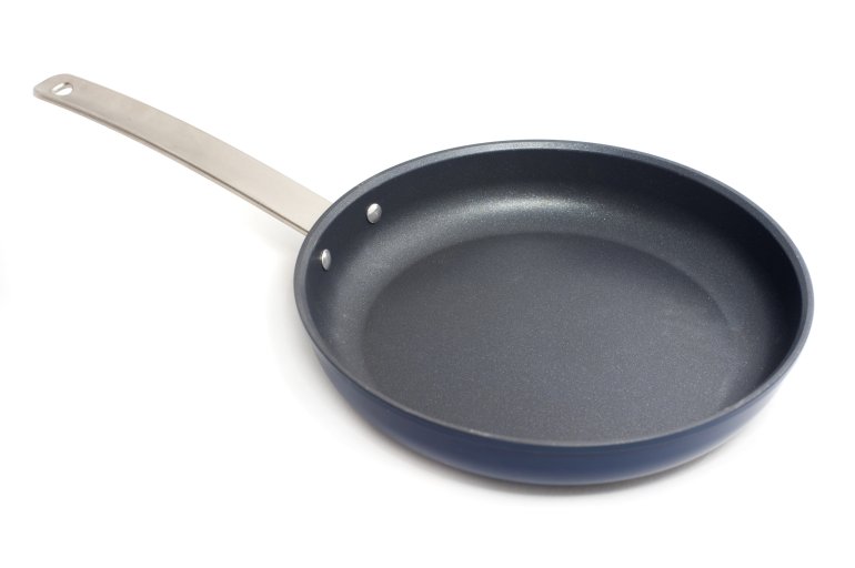 Clean empty circular non-stick frying pan with a metal handle on white arranged diagonally through the frame with copy space