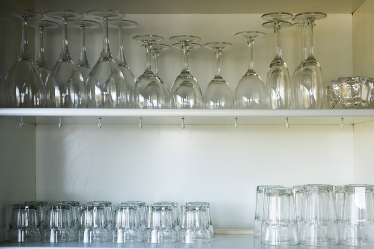 Clean glassware neatly arranged on open white wooden shelves for serving assorted beverages