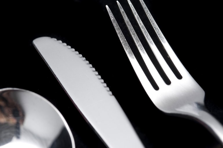 Clean silver metal knife and fork in a close up cropped view on a black table in a dining and food concept