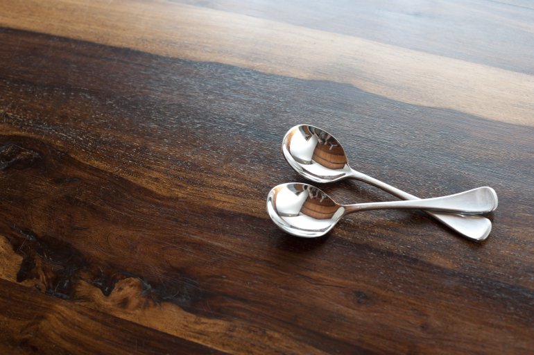 Two silver soup spoons arranged with crossed handles to the side on wood with copy space