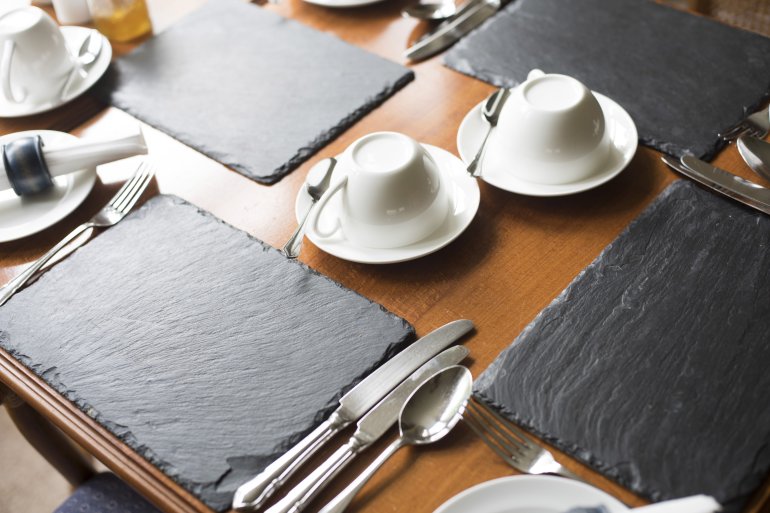 Dinner table settings with slate mats, cutlery, serviettes and coffee cups in an upmarket restaurant
