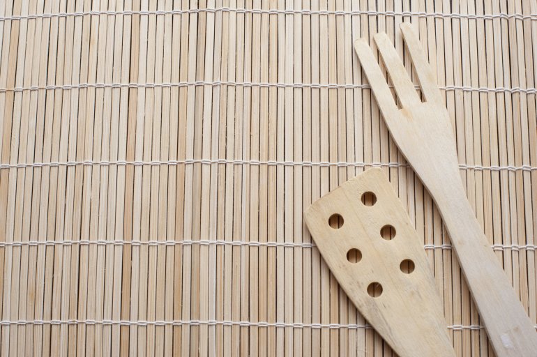 Plain wooden salad fork and spatula arranged to the side in the corner on a bamboo mat with empty space alongside