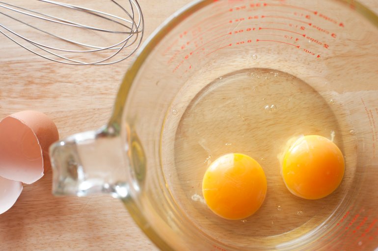 Overhead view of two healthy yellow egg yolks broken into the bottom of a clear glass measuring jug on a kitchen counter to be used as a breakfast or baking ingredient
