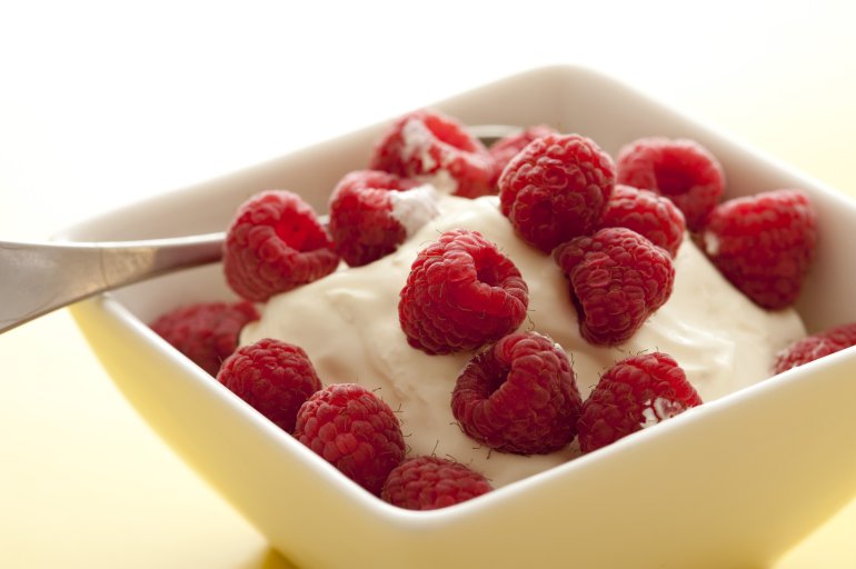 Fresh ripe red raspberries served as a topping on a bowl of thick creamy yoghurt for a tasty healthy breakfast