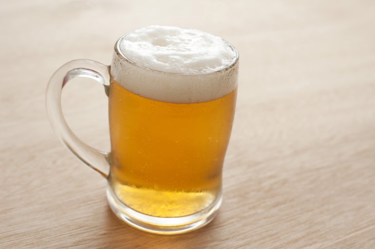 Large cold clear glass tankard of frothy beer, draft or lager standing on a wooden pub or bar counter with copyspace