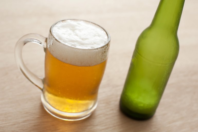 Close up high angle view of a glass tankard and unlabelled green bottle of cold beer on a wooden bar counter