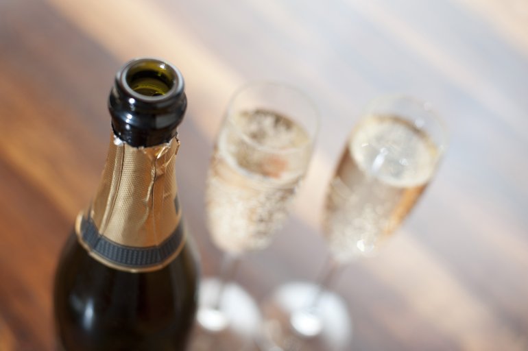 Close up of the neck of an open champagne bottle with full glasses or flutes alongside for a romantic evening or to toast a special event