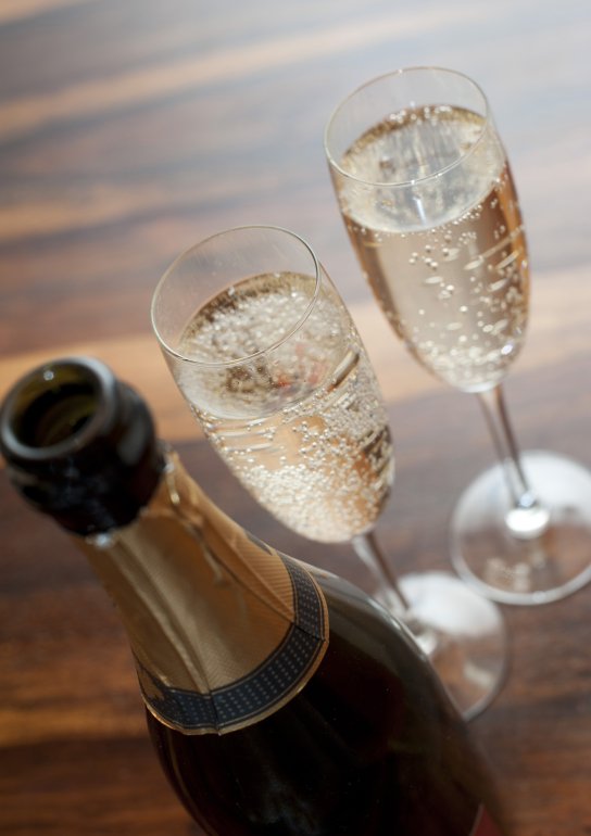 Two flutes of romantic sparkling white champagne standing alongside a champagne bottle on a wooden table ready to celebrate a special occasion, close up high angle view
