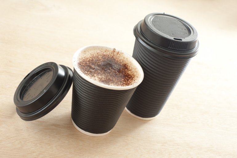 Two takeaway coffees in plastic or paper disposable cups, one with the lid open to display the beverage, one closed, on yellow