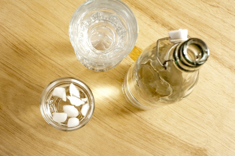 Iced water dispensed into a tumbler from a glass bottle with a resealable cap, view from above on a wooden table in a healthy drink and diet concept