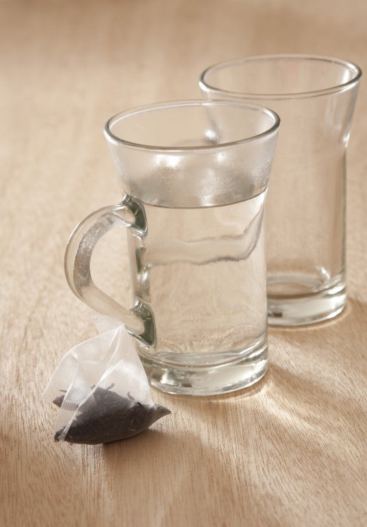 Glass mug filled with boiling water with a dry teabag standing ready alongside to prepare a fresh cup of aromatic relaxing tea