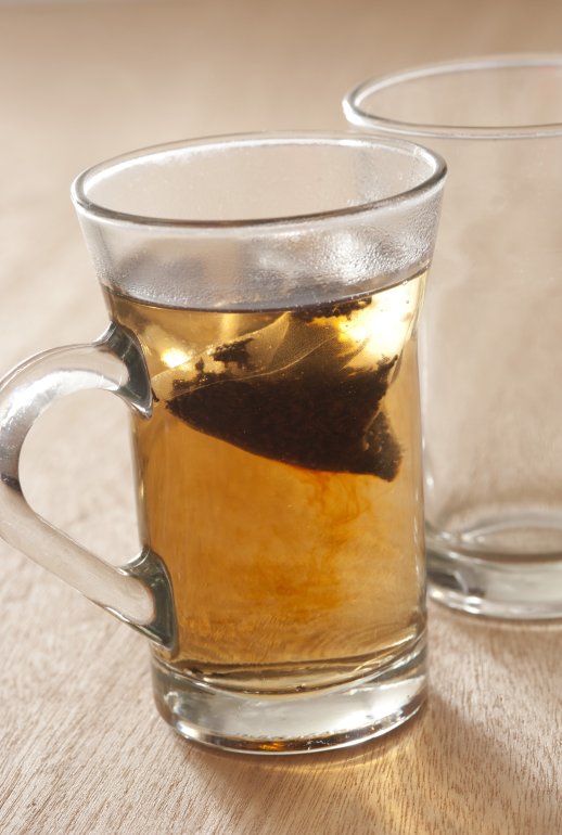 Teabag steeping in boiling water in a clear glass mug brewing a refreshing cup of tea, close up view