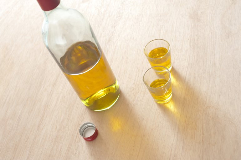 Two shots of whiskey served in small shot glasses with a half full opened bottle alongside, high angle view on a wooden table