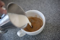 Pouring frothy steamed milk into coffee