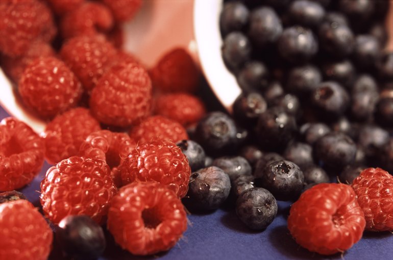 Fresh ripe succulent raspberries and blackcurrants spilling out of ceramic containers, closeup view of whole fruit