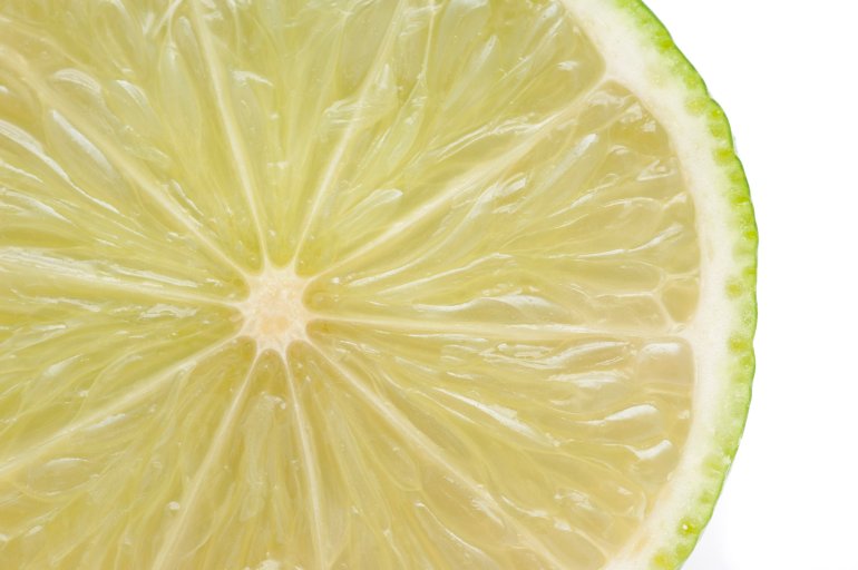 Close up texture of fresh sliced lime showing the juicy pulp, segments and thin bitter rind isolated in white