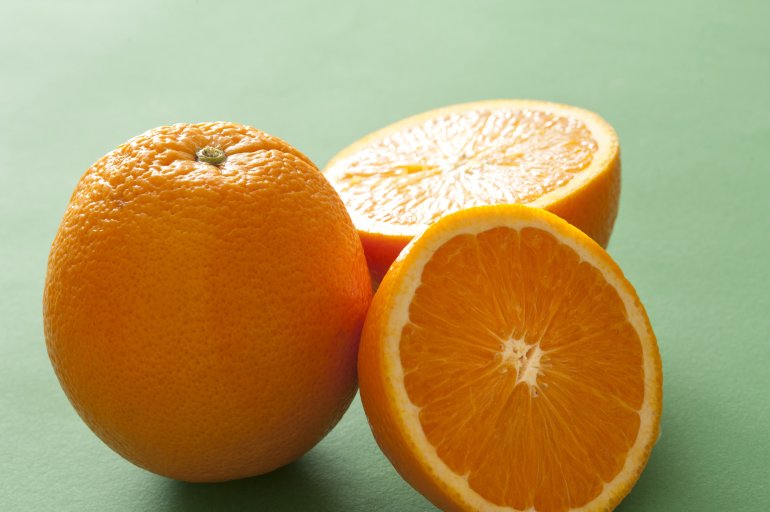 Still life of one whole orange and two halves of cut orange on green background