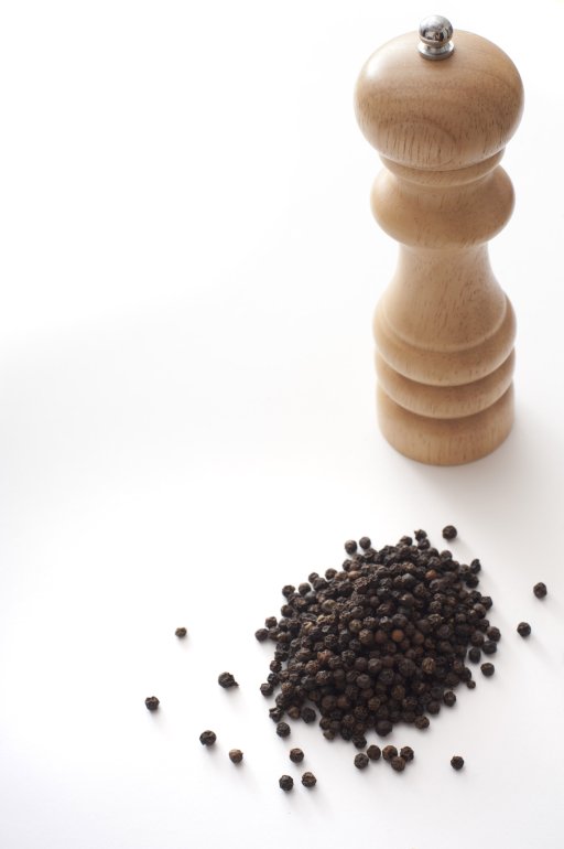 Black peppercorns alongside a wooden grinder or pepper mill isolated on white with copy space for culinary themes