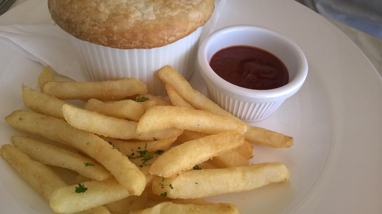Portion of French fries served with a pie and savory dipping sauce on a white plate for a traditional pub lunch