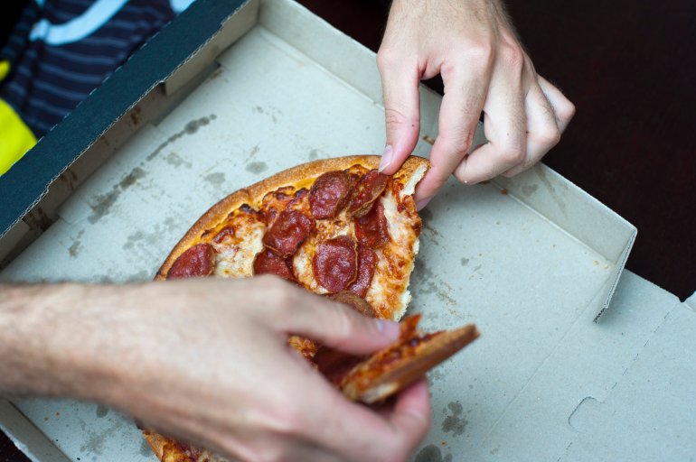 Hands of a hungry man eating a takeaway pepperoni pizza on a traditional disposable cardboard pizza box