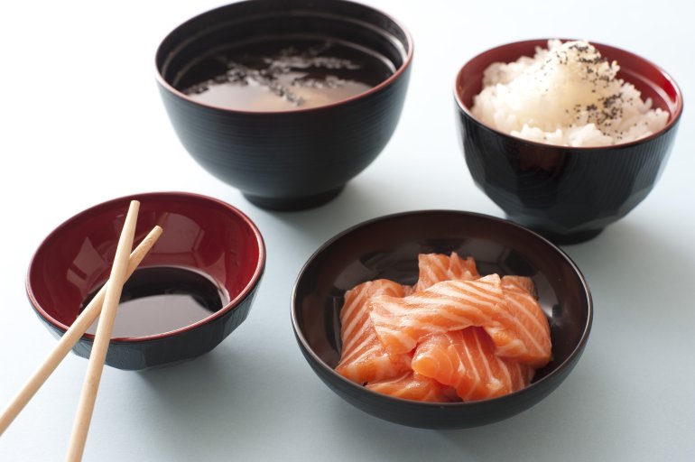 Raw salmon sashimi with soy sauce and a side dish of rice served with Asian chopsticks in individual bowls
