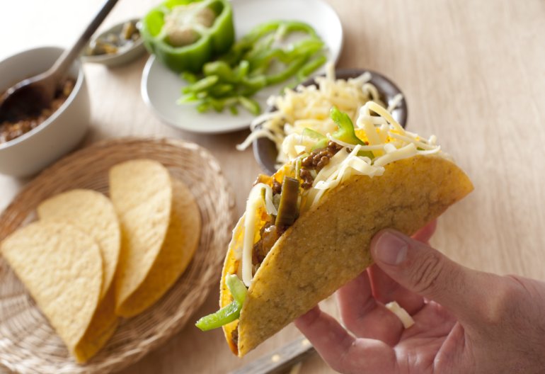 Man preparing a ground beef taco adding fresh green peppers and grated cheese for a tasty lunchtime snack