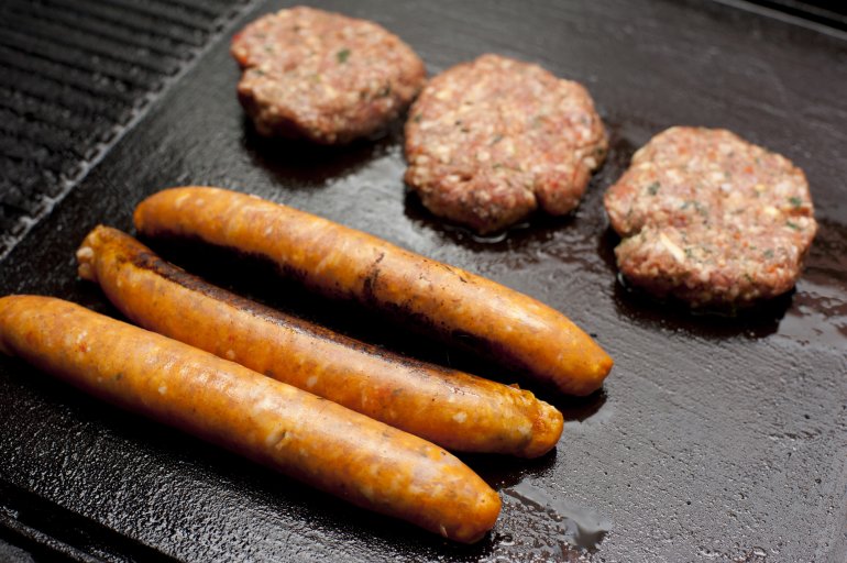 Raw meat rissoles and sausages on grill