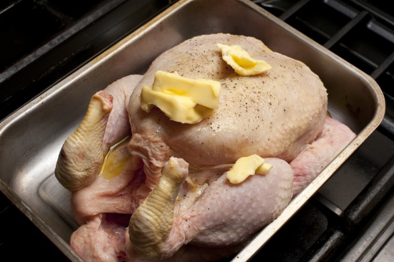 Fresh whole raw chicken seasoned with spices and daubed with butter standing in an oven roasting pan ready for roasting