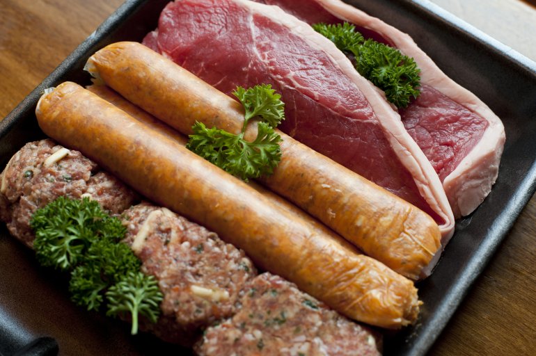 Raw sausages, joints of beefsteak and meat rissoles with fresh parsley lying in pan