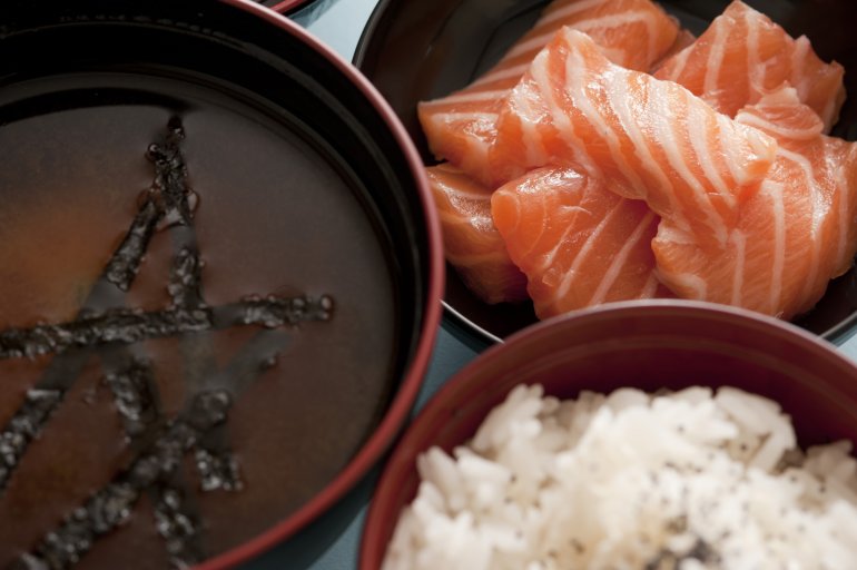 Bowls of freshly prepared Japenese cuisine consisting of bowls of delicious miso soup, raw salmon and white rice close up