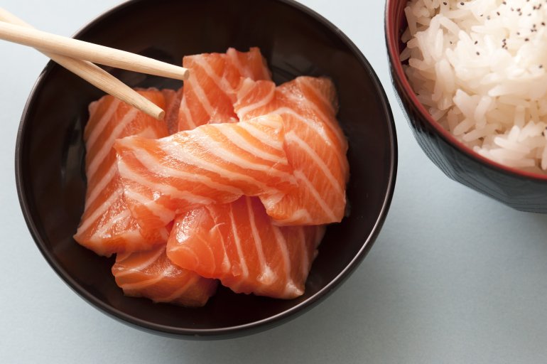 Close up view on raw pink salmon pices in little bowl with wooden chopsticks and herbed white rice